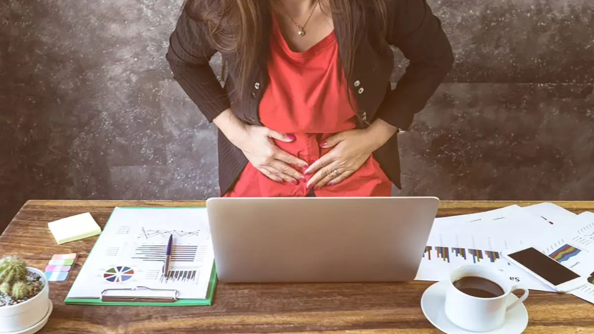 hispanic woman with abdominal pain sitting at her desk at work