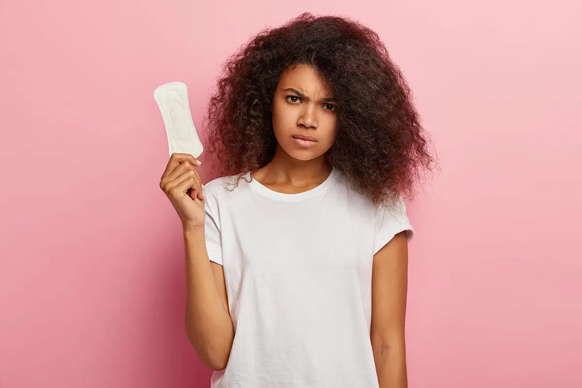 Mujer sosteniendo una toalla sanitaria cuestionando el flujo vaginal y los fibromas